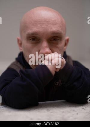 Primo piano di un uomo pensivo con nanismo, mani strette, copertura del mento e visione della fotocamera, appoggiato su un parapetto. Persona unica con un focus Foto Stock