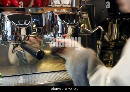 Il barista prepara l'espresso con una macchina da caffè cromata al Cafeteria Triple Five, mostrando movimento e riflessi della vita del caffè. Foto Stock