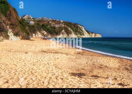Byala, Bulgaria - 25 settembre 2025: Persone che si rilassano e camminano sulla spiaggia sabbiosa vicino a ripide scogliere bianche in un giorno d'estate soleggiato sulla costa del Mar Nero. Foto Stock