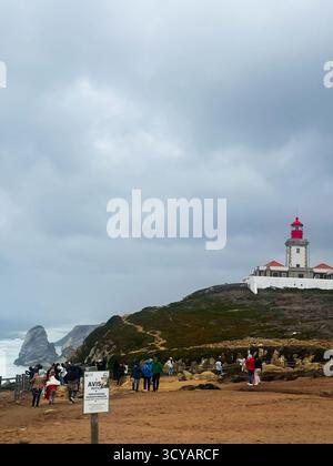 Colares, Portogallo - 28 settembre 2025: Faro di Cabo da Roca, Portogallo, con gruppi di visitatori che esplorano la costa sotto un cielo nuvoloso. Foto Stock