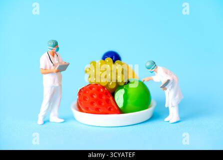 Vista ravvicinata di scienziati in miniatura che esaminano frutti geneticamente modificati colorati in un laboratorio; colori vivaci e design intricati evidenziano la bioengina Foto Stock