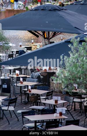 Terrazza all'aperto con ombrelloni neri, tavoli vuoti e sedie lungo l'acqua a Leida, Paesi Bassi, con un'accogliente disposizione per pranzare e scaldavivande Foto Stock