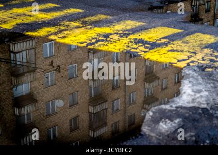 Costruire riflessi in una pozzanghera accanto alla segnaletica stradale gialla usurata. Foto Stock