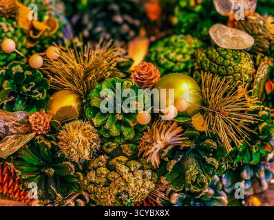 Primo piano sulla vivace corona di Natale: Sfavillanti coni di pino verde, baule dorate, fiori autunnali. Decorazioni natalizie e design marketing di stagione Foto Stock