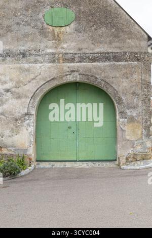 Facciata in pietra intemprata caratterizzata da una grande entrata ad arco con una vibrante doppia porta verde Foto Stock