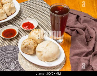 2 panini fritti in padella e 1 panino di maiale al pepe con salse da immersione e un alto bicchiere di tè freddo isolato sul tovagliolo vista laterale del cibo dim sum di taiwan Foto Stock