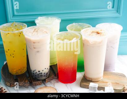 Il tè freddo assortito include frutto della passione, perla, taro, melograno, menta, lime, latte, frumento, germe e cubetti di ghiaccio in alto bicchiere serviti su un asse di legno Foto Stock
