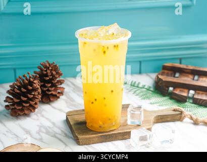 Tè verde freddo alla frutta della passione con cubetti di ghiaccio in alto vetro servito su una tavola di legno con vista laterale della bevanda fredda di taiwan Foto Stock