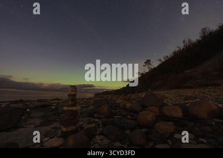 Un tranquillo paesaggio notturno sulla costa rocciosa di Paldiski, Estonia, caratterizzato da cairn di pietra sotto un cielo stellato con l'aurora boreale. Foto Stock