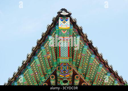 Tetto decorato del tempio coreano con motivi che si affacciano su un cielo azzurro Foto Stock