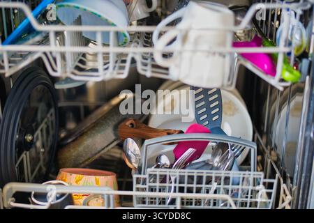 Vista interna della lavastoviglie carica con stoviglie, utensili e pentole assortiti pronti per il ciclo di pulizia Foto Stock