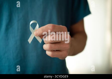 Primo piano di un uomo che tiene in mano un nastro blu. Simbolo della consapevolezza del cancro alla prostata a novembre, assistenza medica, diagnosi precoce, cure oncologiche e supporto familiare. Foto Stock