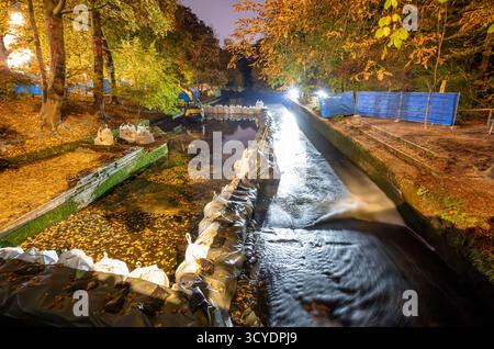 Monaco, Germania. 18 ottobre 2025. Decine di sacchi di sabbia e una macchina da costruzione si trovano nella parte inferiore dell'Eisbach parzialmente drenato nel giardino inglese. Attualmente non è più possibile praticare surf sull'Eisbach, poiché la pulizia annuale del torrente ha iniziato a ripulire il fondo. L'onda di Eisbach è un punto di riferimento per i surfisti ricreativi. Crediti: Peter Kneffel/dpa/Alamy Live News Foto Stock