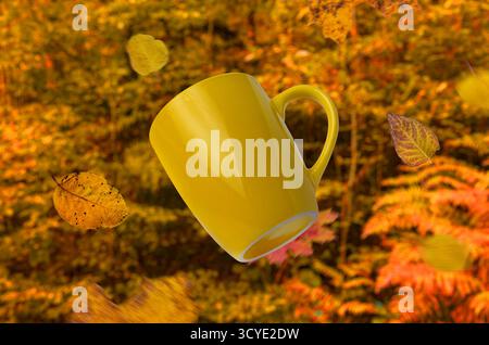 Tazza da caffè gialla circondata da foglie cadenti e da una foresta dorata calda, perfetta idea autunnale per design e pubblicità Foto Stock