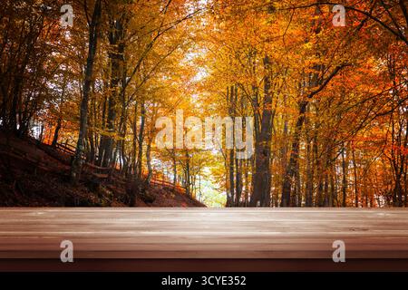 Tavolo in legno di fronte alla colorata foresta autunnale, sfondo perfetto per i design stagionali, la presentazione dei prodotti o le promozioni autunnali Foto Stock