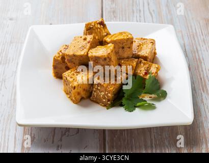 Cubetti di tofu marinati piccanti con salsa salata, semi di sesamo e coriandolo serviti nel piatto sul tavolo di legno vista ravvicinata del cibo di Hong Kong Foto Stock