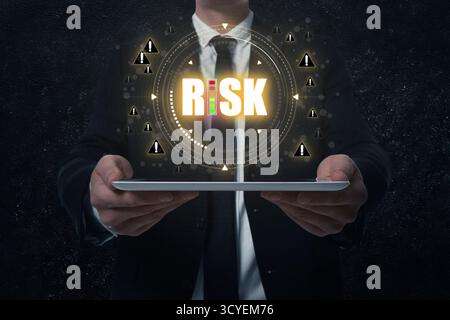 Uomo d'affari che tiene un tablet su sfondo nero, primo piano. Rischio di parola circondato da cartelli di avvertenza sopra il dispositivo Foto Stock
