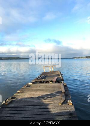 Tranquillo molo in legno che si estende su un tranquillo lago sotto un cielo parzialmente nuvoloso, offrendo un tranquillo rifugio sul lago. Foto Stock