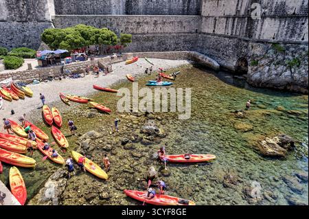 I turisti lanciano kayak da una spiaggia rocciosa sotto le storiche mura della città di Dubrovnik, una popolare attività avventurosa sul mare Adriatico. Foto Stock