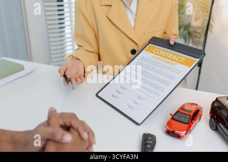 Una negoziazione per la vendita di auto si svolge in un ufficio in cui una donna venditrice con un blazer giallo spiega i dettagli di un contratto a un cliente maschio, showin Foto Stock