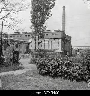 Questa foto d'archivio degli anni '1970 cattura un paesaggio industriale classico presso la fabbrica di armature e isolatori di Slavyansk (AIF) a Sloviansk, RSS Ucraina. L'immagine presenta una grande officina di mattoni, un'alta cisterna e una rete di condotte sopraelevate. È visibile un segnale di attraversamento della ferrovia. In primo piano, un segno propagandistico recita parzialmente "MIR TRUD" (pace, lavoro). Questo colpo racchiude il potere industriale dell'era sovietica, una caratteristica del pacifico Donbas. Foto Stock