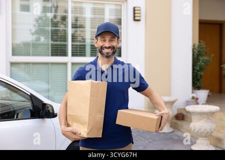 Corriere automatico maschio sorridente in piedi con pacchetti che guardano alla fotocamera Foto Stock