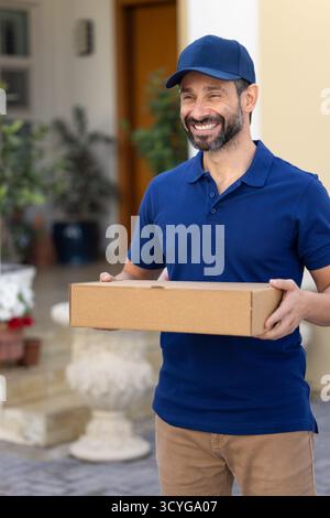 Corriere sorridente in uniforme in piedi nel cortile di casa di lusso Foto Stock