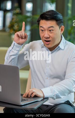 Eureka. Un uomo d'affari cinese attento e intelligente che utilizza il laptop fa alzare il dito con un piano creativo si sente entusiasta di una domanda motivazionale di ispirazione per una buona idea nella hall dell'hotel. Foto Stock