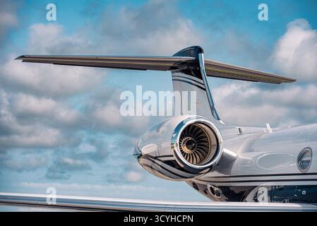 Primo piano di una moderna coda di un jet business e di un motore turbofan che mostrano un design aerodinamico e pale della ventola ad alto bypass sotto cieli parzialmente nuvolosi. Foto Stock