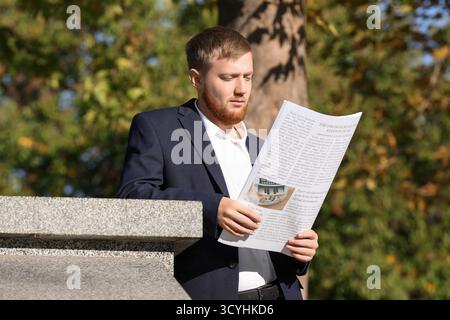 Giovane imprenditore quotidiano di lettura in posizione di parcheggio Foto Stock
