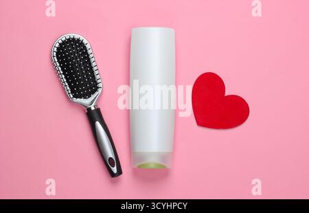 Bottiglia di shampoo, spazzola con cuori su sfondo rosa pastello. Bellezza e cura dei capelli. Vista dall'alto. Minimalismo Foto Stock