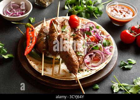 Kebab lula grigliato con verdure fresche su pane piatto su vassoio di legno su sfondo in pietra nera. Vista ravvicinata Foto Stock