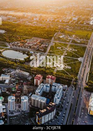 Ripresa aerea verticale di Bishkek all'alba o al tramonto, mostrando un grande parco urbano, appartamenti moderni e una foschia dorata Foto Stock