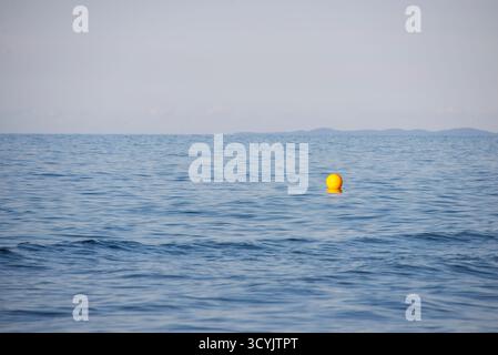 Una boa gialla luminosa galleggia sulle calme acque blu del mare, con dolci increspature che la circondano. L'orizzonte sullo sfondo mostra un debole outlin Foto Stock
