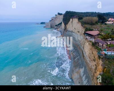 Vista aerea di Loggas Beach, Peroulades, Corfù. Un famoso bar e ristorante sulla scogliera si trova sul bordo di spettacolari scogliere a stratificate sul mare Foto Stock
