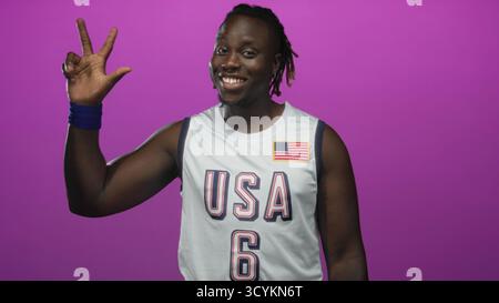 La maglia da basket Man in usa mostra i pollici e la mano alzata in studio con sfondo magenta; celebrazione della fiducia. Foto Stock