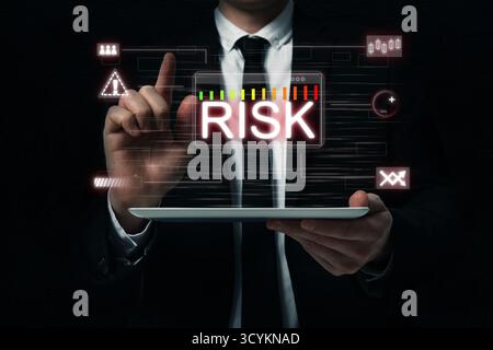 Uomo d'affari che tiene un tablet e utilizza lo schermo virtuale sopra il dispositivo con la parola rischio e diverse icone nelle tenebre e primo piano Foto Stock