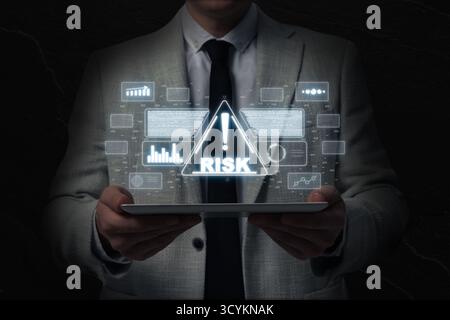 Uomo d'affari che tiene un tablet nel buio, primo piano. Cartello di avvertimento con la parola rischio e dati sopra il dispositivo Foto Stock