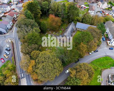 Vista aerea di una chiesa e del suo cimitero circondati da alberi autunnali in Galles Foto Stock