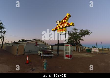 Motel sulla strada con un cartello al neon intempestivo e un'auto arrugginita parcheggiata davanti, evocando la nostalgia americana nel paesaggio desertico del sud-ovest. Foto Stock