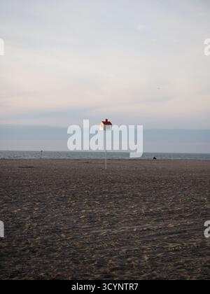 Spiaggia invernale minimalista a Deauville, Francia, con un piccolo cartello con tetto rosso sotto il cielo pastello Foto Stock