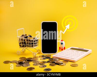 Smartphone con schermo vuoto con carrello pieno di monete, calcolatrice, razzo e icona di destinazione su sfondo giallo, che rappresenta lo shopping online e la vendita Foto Stock