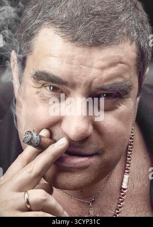 Questo straordinario ritratto cattura una figura mafiosa che fuma con sicurezza un sigaro. L'uomo mostra una presenza alfa, circondata da un misterioso buio Foto Stock