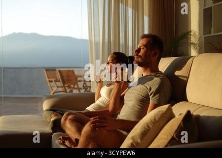 Una coppia rilassante bevendo un caffè dopo lo yoga seduti sul divano di casa al tramonto Foto Stock