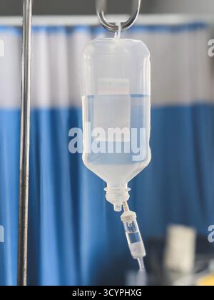 Foto ravvicinata di un flacone di gocciolamento IV medico riempito di liquido trasparente appeso in una stanza d'ospedale. Apparecchiature sanitarie utilizzate per l'idratazione dei pazienti Foto Stock