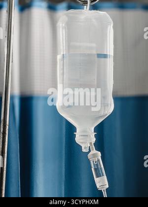 Foto ravvicinata di un flacone di gocciolamento IV medico riempito di liquido trasparente appeso in una stanza d'ospedale. Apparecchiature sanitarie utilizzate per l'idratazione dei pazienti Foto Stock