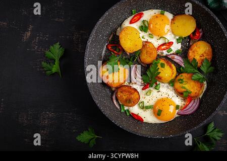 Uova e patate fritte con cipolle e peperoncino in uno sfondo rustico. Vista dall'alto Foto Stock