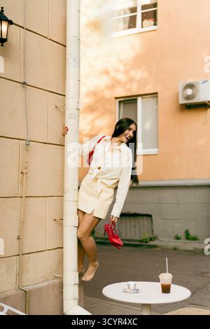 Donna giocosa che ride a piedi nudi con tacchi alti rossi per strada urbana Foto Stock