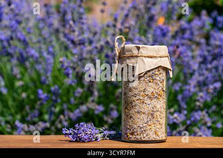 Sale marino himalayano con lavanda secca e fiori di camomilla in vaso di vetro lo sfondo dei fiori di lavanda su un tavolo di legno nelle soleggiate giornate estive. Naturale b Foto Stock