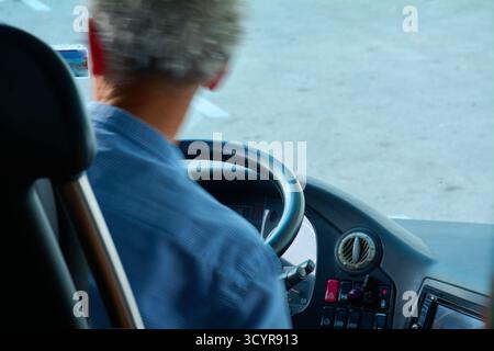 Dubrovnik. Croazia - 20 ottobre 2025: Un autista di autobus non riconosciuto, visto da dietro, siede al posto di guida. La luce del sole illumina le braccia e il grigio Foto Stock